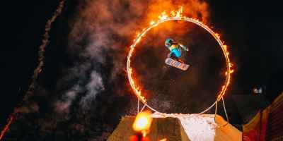 man jumping on snowboard through fire circle at night