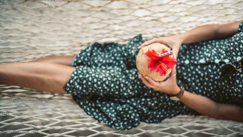 woman in green and white polka dot dress lying on a hammock with fresh coconut juice