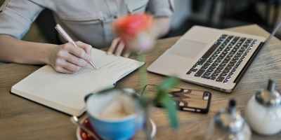 person writing on a notebook beside macbook
